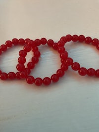 three red glass bead bracelets on a white surface